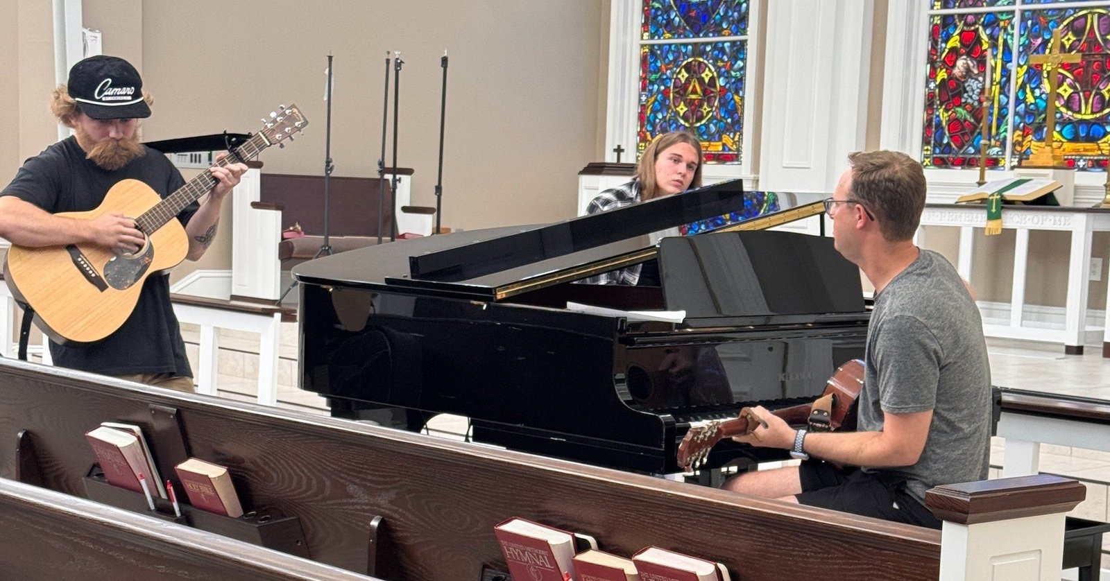 Three songwriters working together around a grand piano in the chapel at Ghost Noise Writing Night